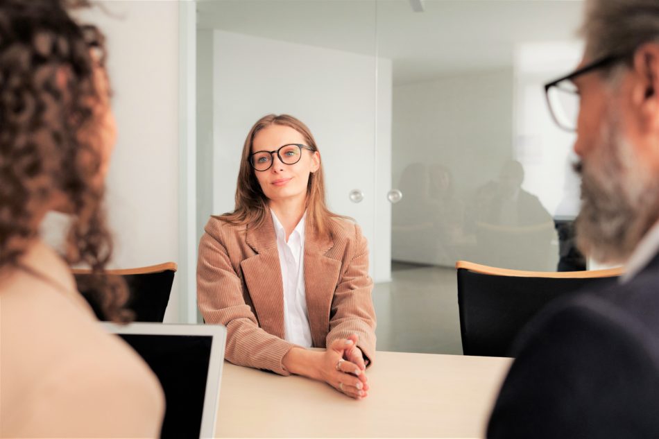 Woman sits and looks at two people during a business interview