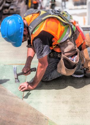 Man works on a roof with a hammer at a construction site