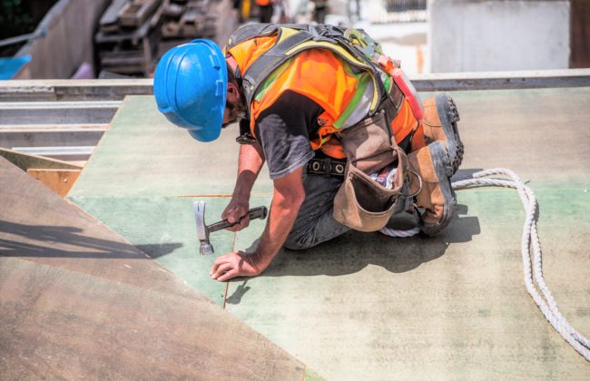 Man works on a roof with a hammer at a construction site