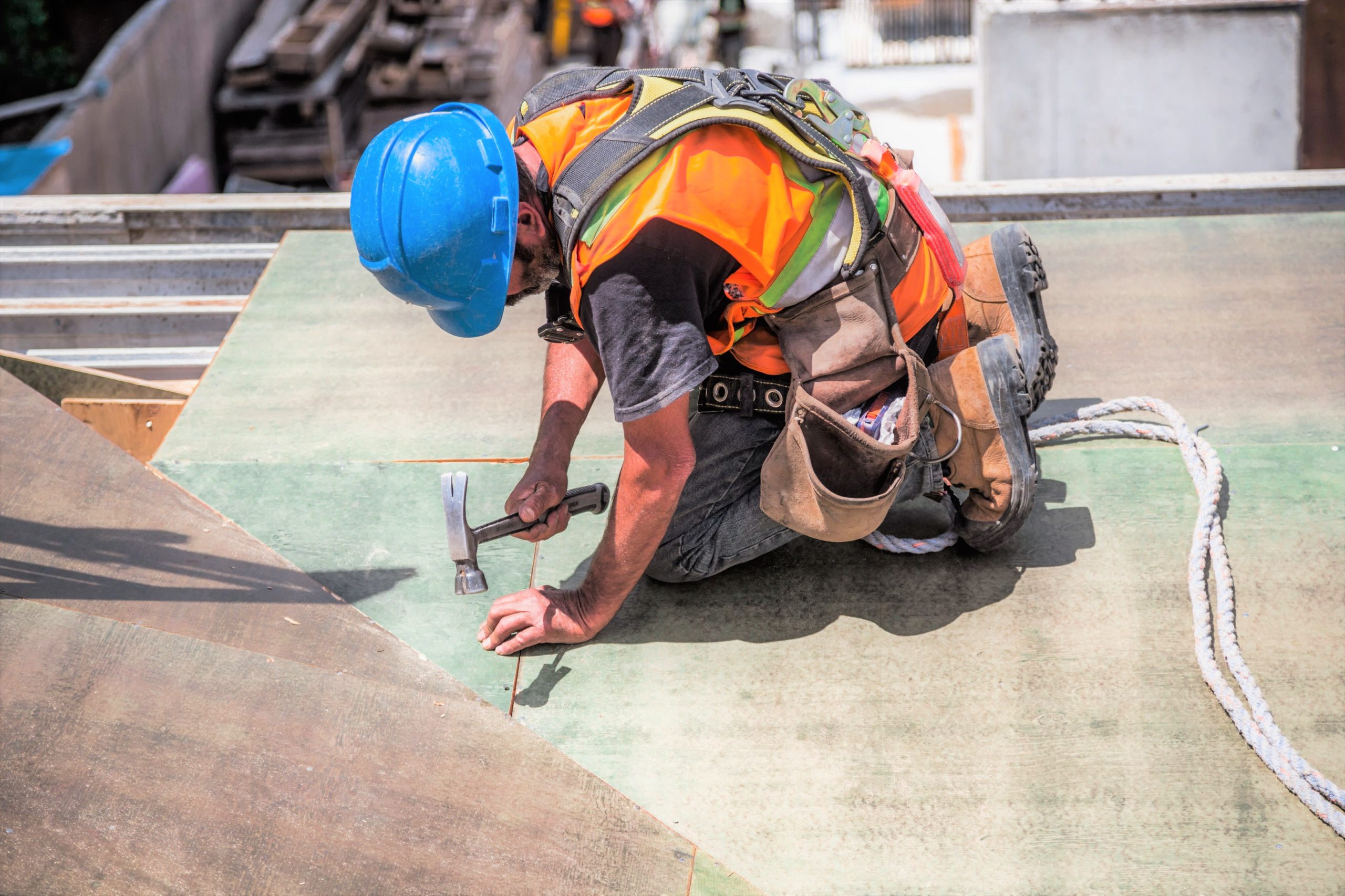 Man works on a roof with a hammer at a construction site