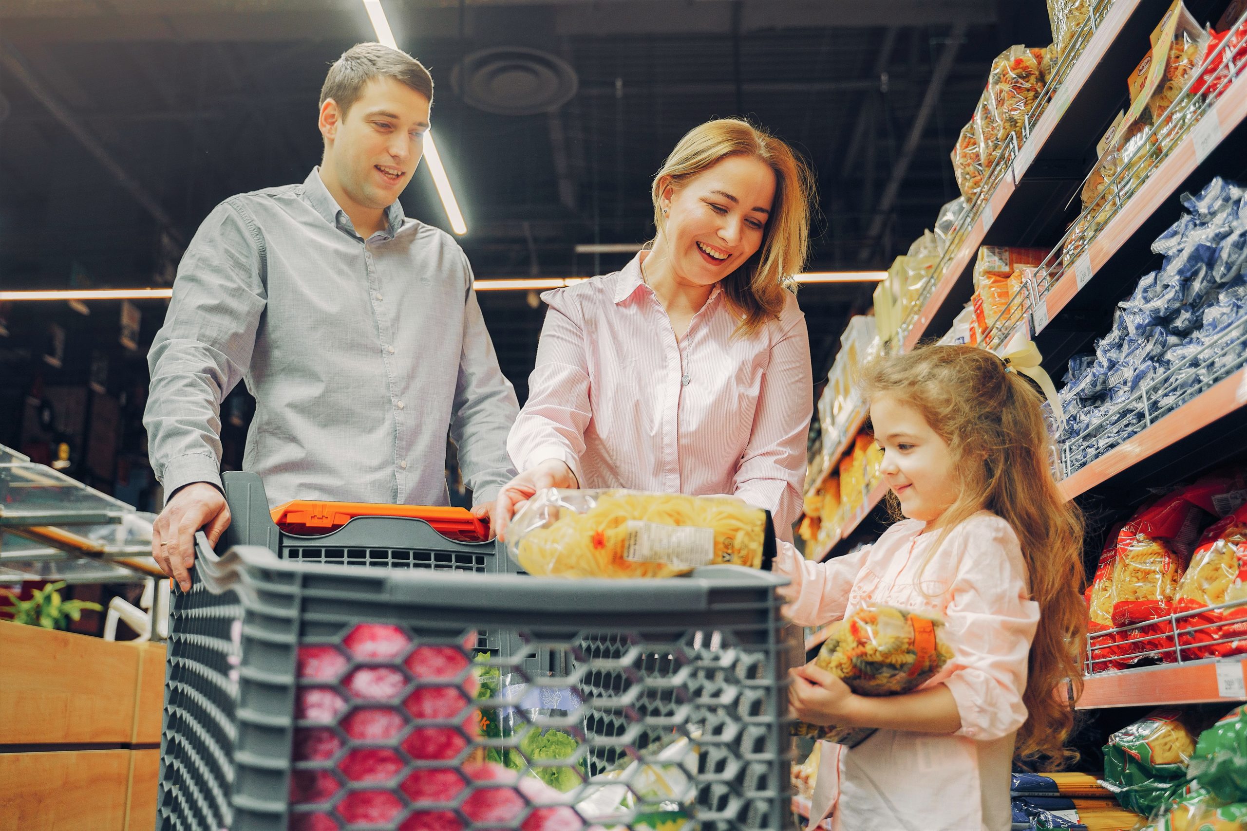 A mum dad and child enjoy a trip to the supermarket where the daughter is putting pasta in the trolley
