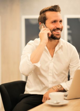 Man answers his phone while sat at his laptop