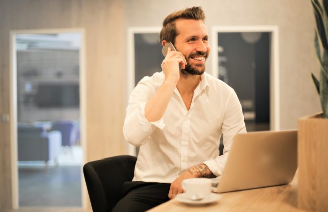 Man answers his phone while sat at his laptop