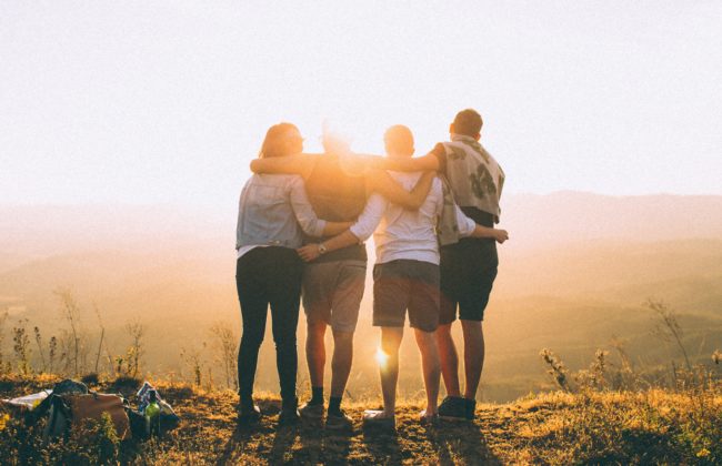 A group of friends stand looking out at the sunset