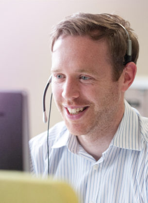 Man speaks into his headset while working at a computer