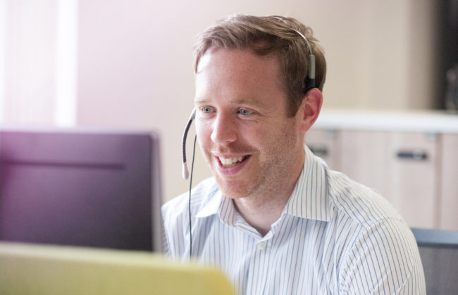 Man speaks into his headset while working at a computer