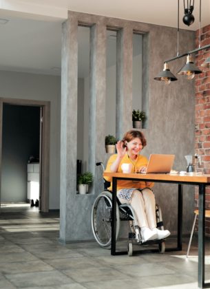 A woman in a wheelchair waving at laptop in online call