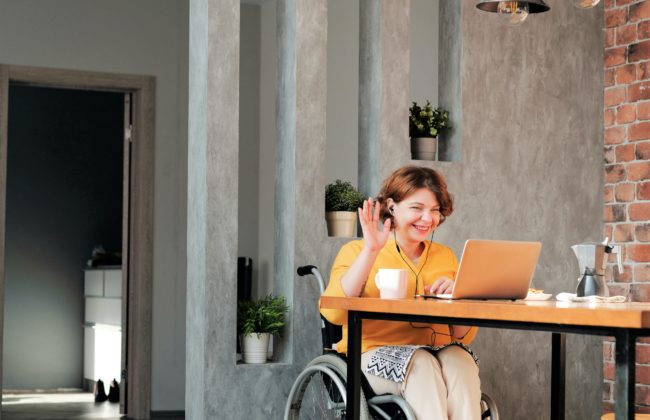 A woman in a wheelchair waving at laptop in online call