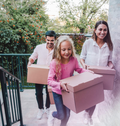 Portrait of happy family with one child moving to new house with cardboard boxes. A young family move into their new home. Smiling family carrying boxes into new home on moving day. Family entering in their new house.