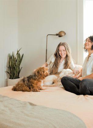 Smiling couple play with their dog on the bed