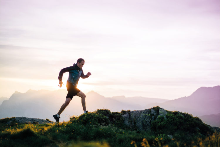 Young man runs on mountain ridge at sunrise