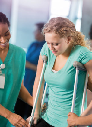 Injured woman is supported by nurses while trying her crutches