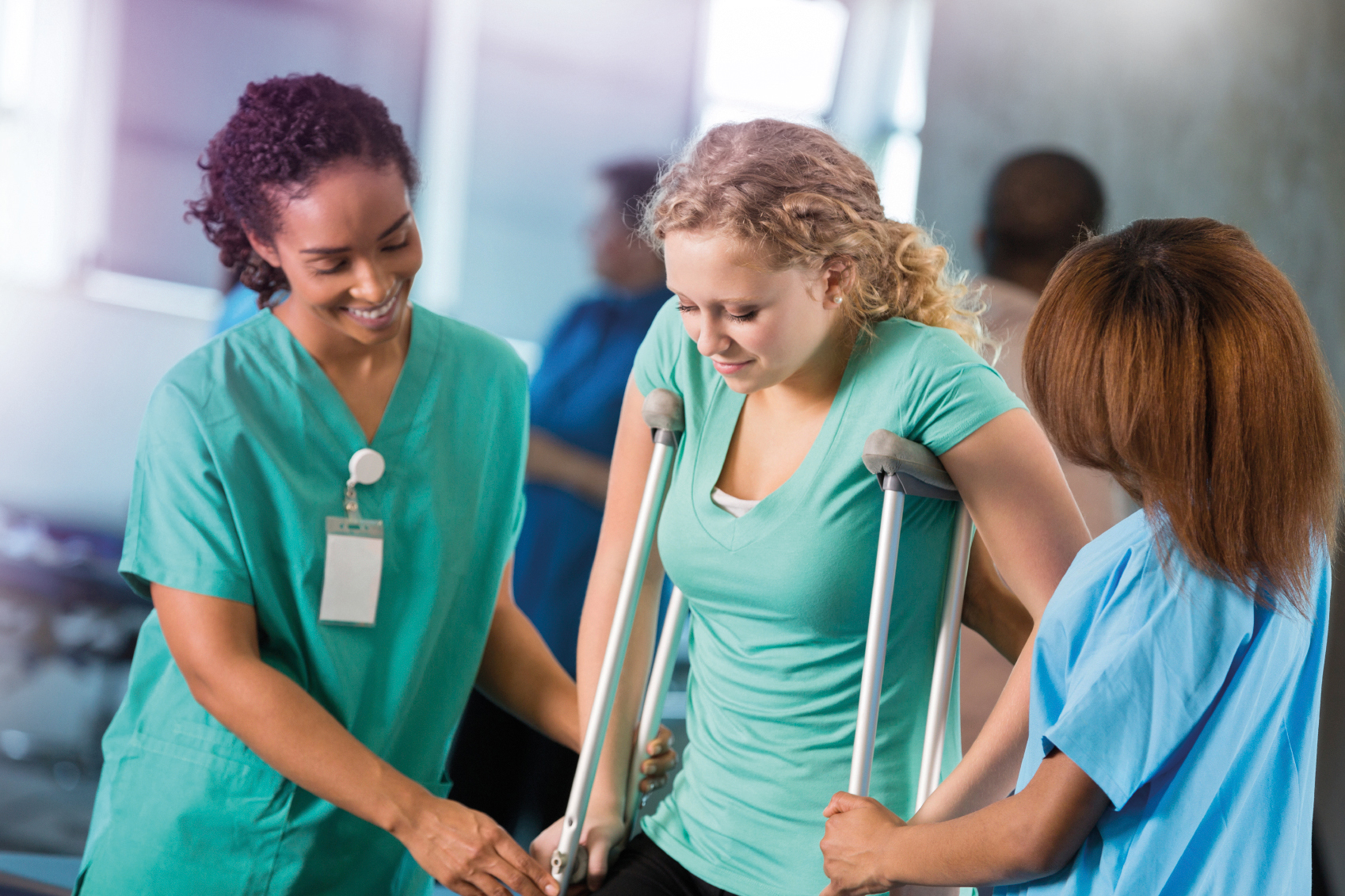Injured woman is supported by nurses while trying her crutches