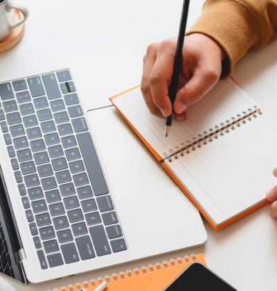 Person writes in notebook while looking at laptop