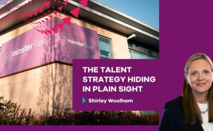 Promotional graphic showing the exterior of a modern office building with a large purple sign reading “minster law solicitors” mounted on the corner. Trees and shrubs are visible in the foreground, with a red triangular pattern overlaying the top left. On the right, a purple panel features a professional headshot of a person wearing a dark blazer and light top. White text reads: “THE TALENT STRATEGY HIDING IN PLAIN SIGHT” with smaller text below: “Shirley Woolham.”